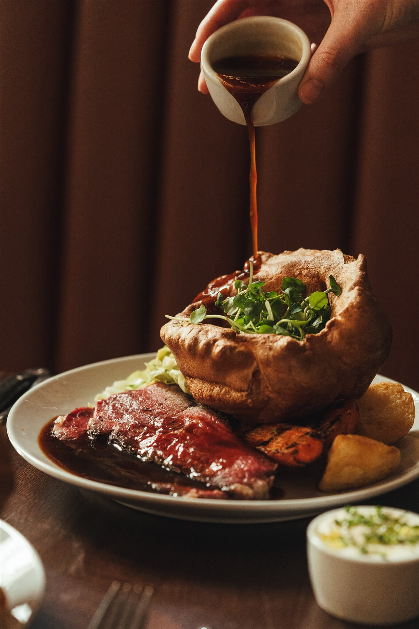 Gravy poured onto sliced roast beef with a Yorkshire pudding